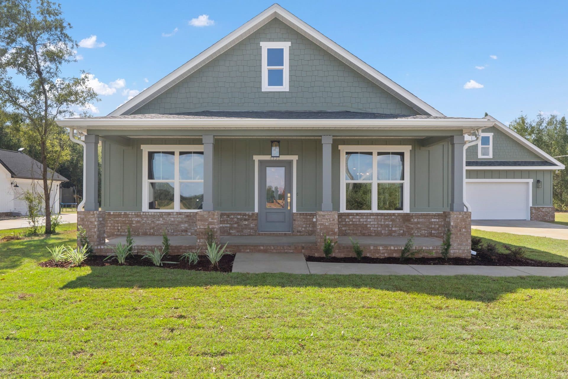 The Ashley, a sage craftsman on a brick water table with a deep front porch