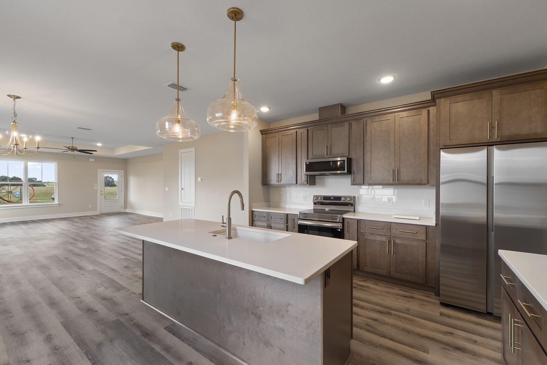 The Ashley kitchen with stained cabinets, a quartz island and glass pendants