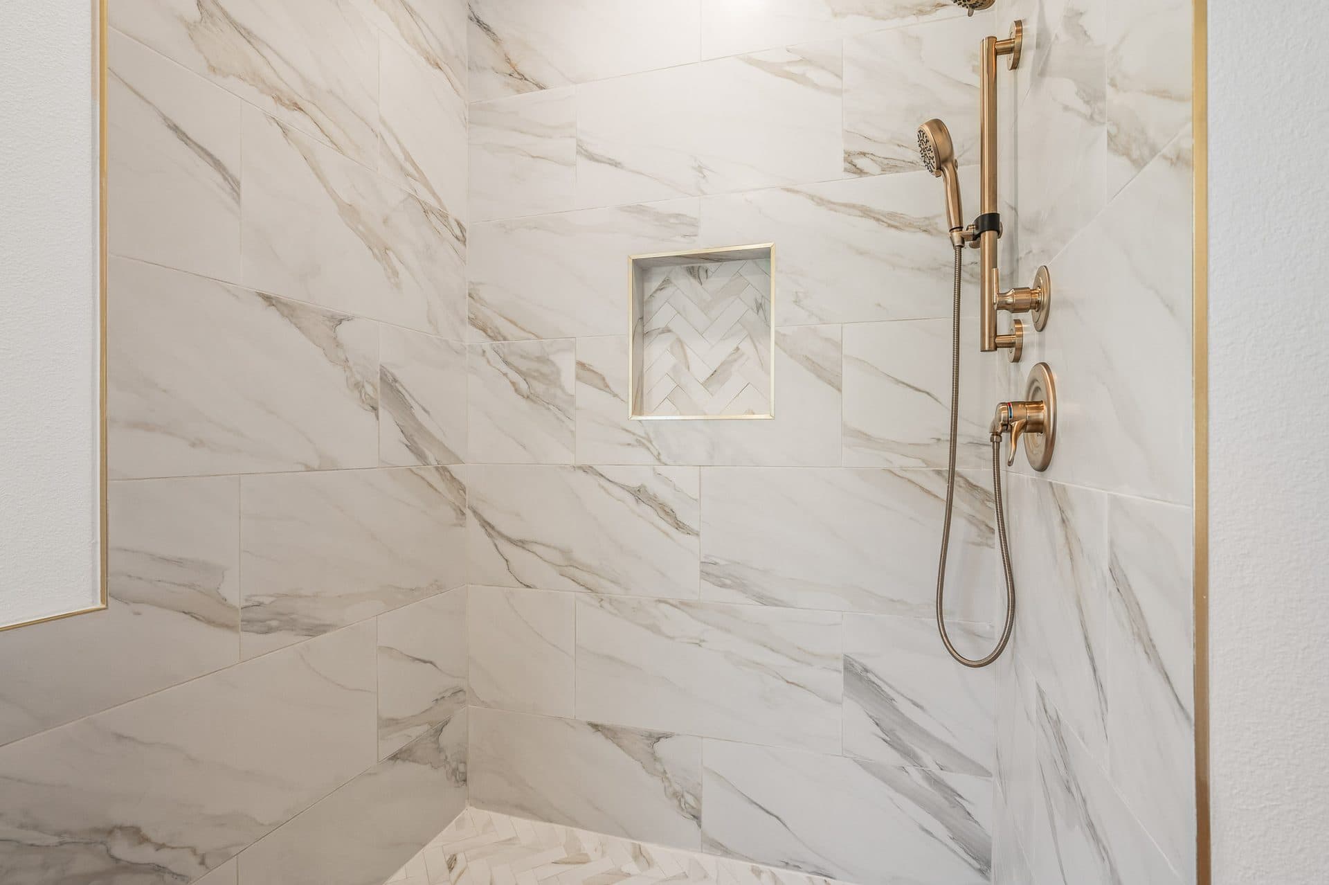 Marble-look tile shower with champagne bronze fixtures in a finished Cameron