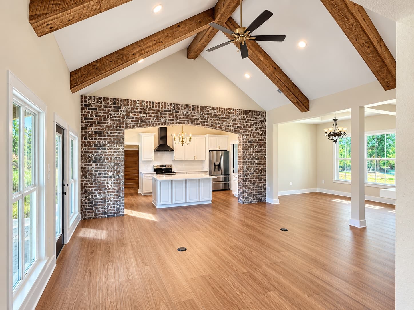 The vaulted great room of a finished Heritage, rough-sawn beams overhead and a brick arch opening to the kitchen