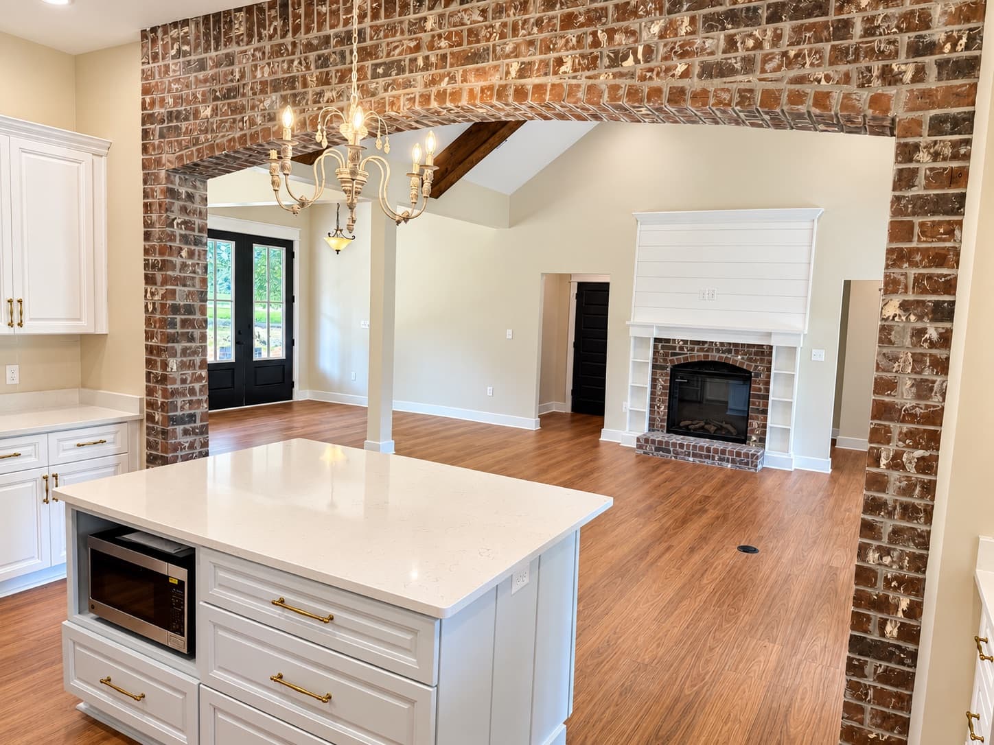 Looking through the brick arch past the white kitchen island to the shiplap fireplace wall with built-in shelves