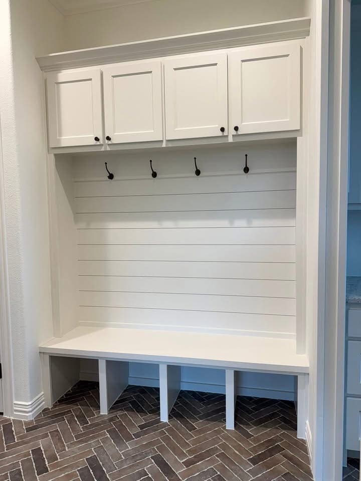 The mud bench off the garage entry, shiplap backer, coat hooks and upper cabinets over a herringbone brick floor