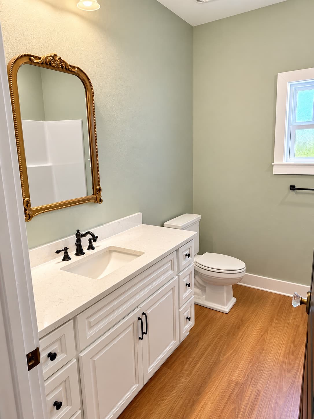 The powder room of a finished Heritage, sage walls, a white vanity with oil-rubbed bronze fixtures and a gilded mirror