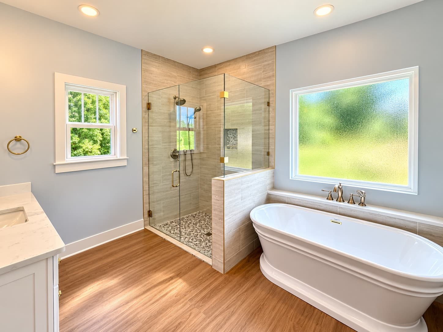 The primary bath of a finished Heritage with a freestanding tub under a window and a frameless glass tile shower with brass hardware