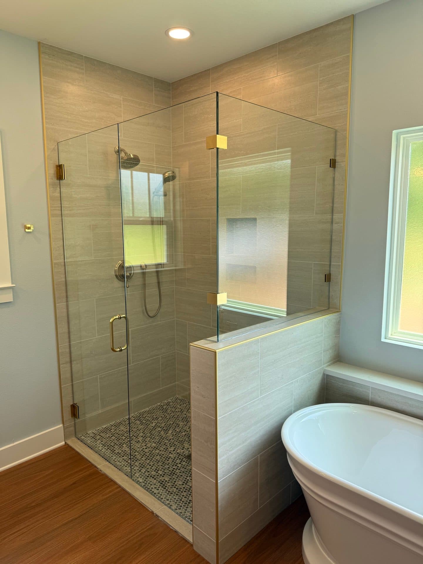 The walk-in tile shower in the Heritage primary bath, with a pebble floor, a niche and brass glass clips