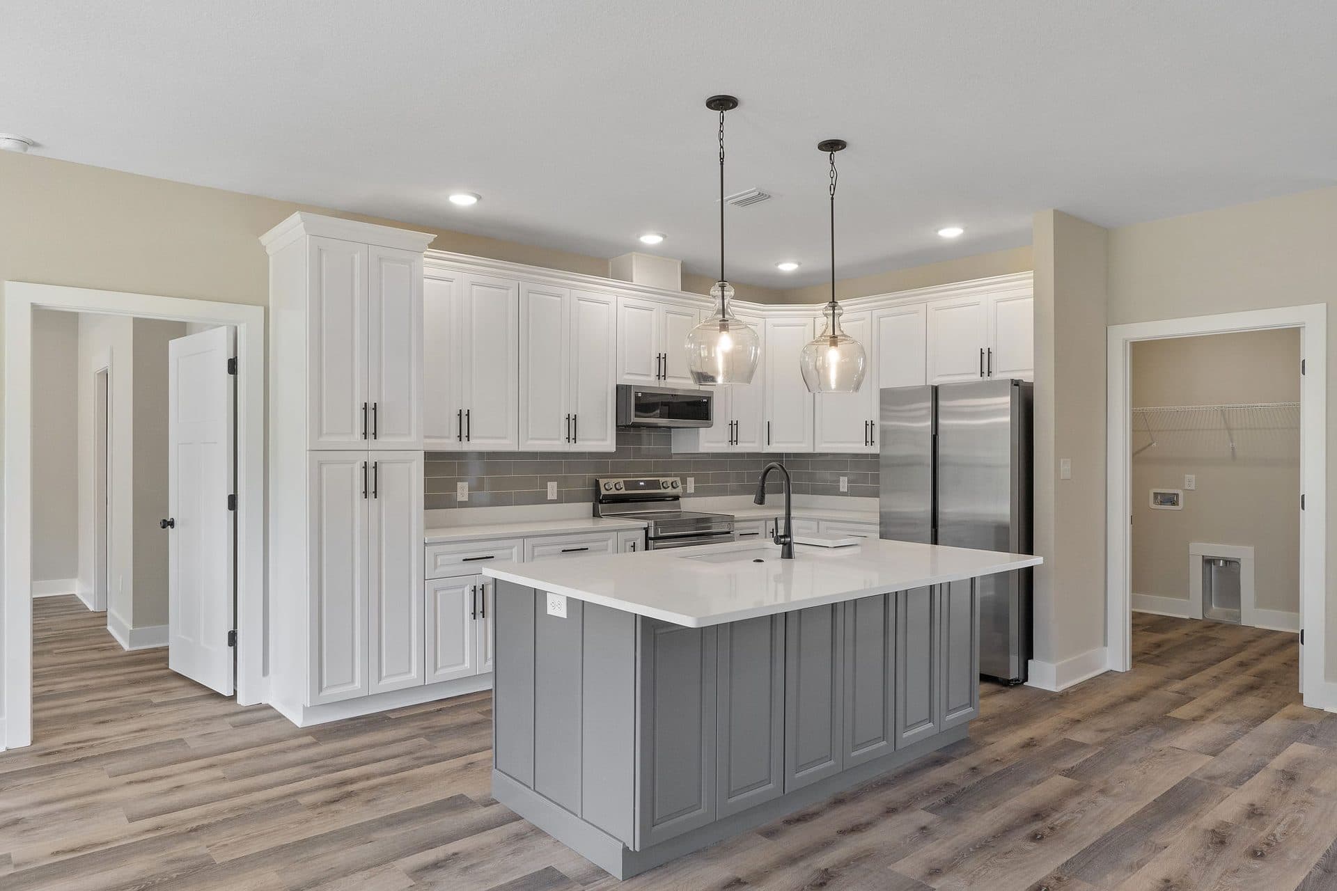 Kitchen of a finished Lunsford with white cabinets, a grey island and glass pendants