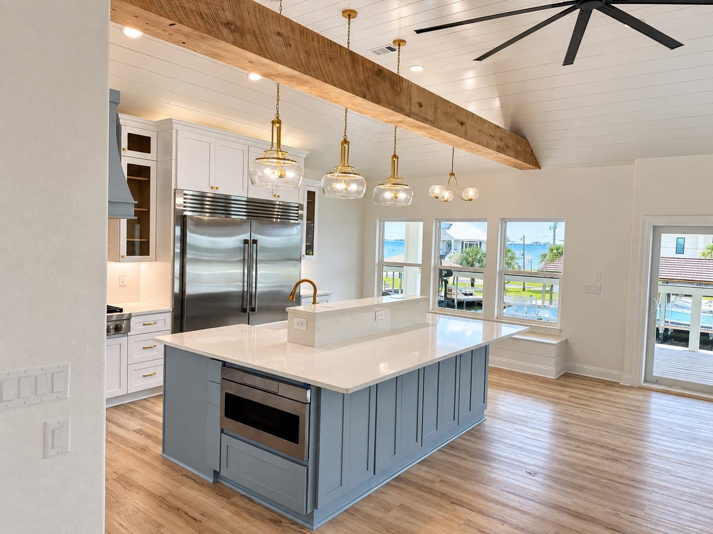 Renovated Gulf Breeze kitchen with a slate blue island, white shaker cabinets, brass pendants and a wall of windows looking out at the bay